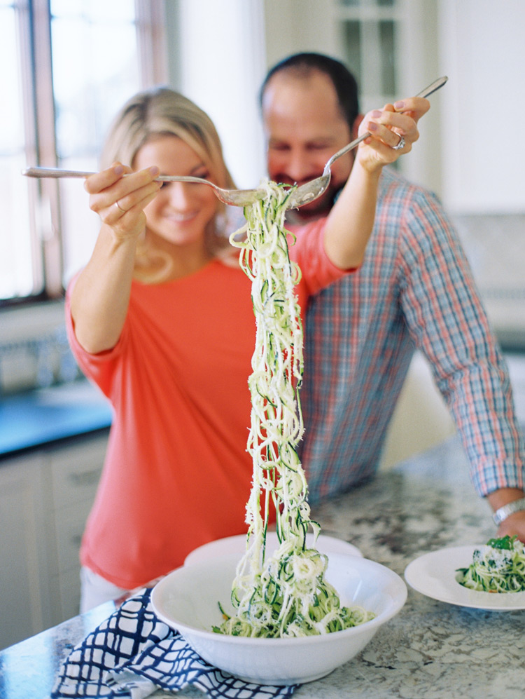 Laughing and cooking together in their beautiful kitchen. Engagement shoot ideas. Zucchini pasta.