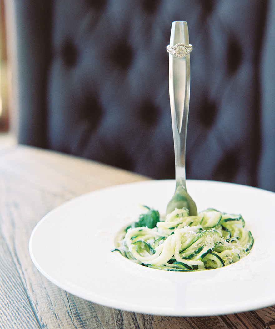 Engagement ring displayed on a fork in a bowl of delicious zucchini pasta. Engagement photo ideas.