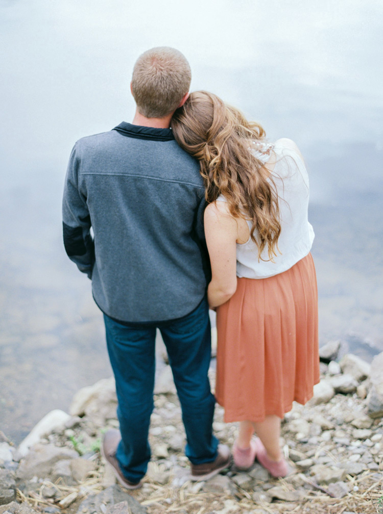 Her head on his shoulder as they gaze at the lake. Colorado lakeside engagement shoot. 