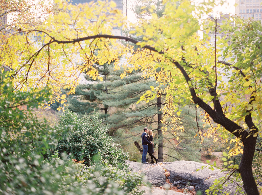 Autumn in New York City's Central Park. A couple embrace in the distance. NYC engagement shoot.