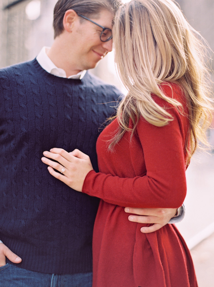 A couple dressed for autumn in cozy sweaters stand in an embrace. New York engagement shoot. 