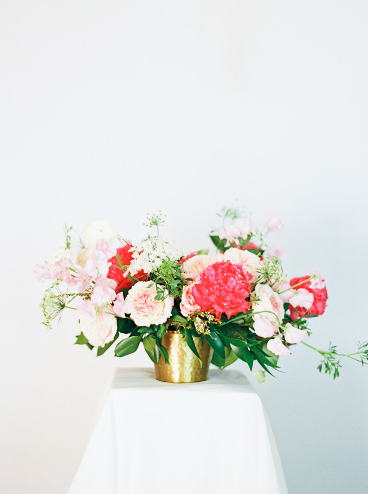 Loose, organic flower design in shades of pink in a low brass basket. Peony, garden rose, sweet pea