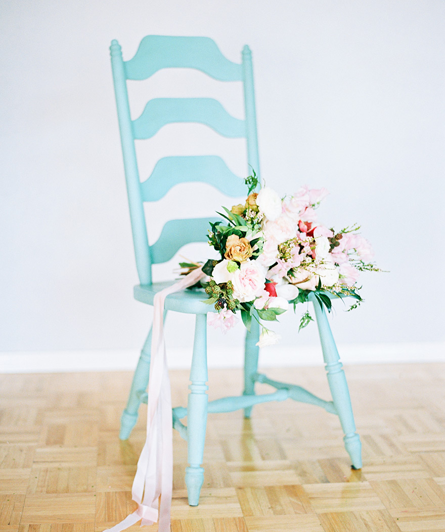 Soft, natural bouquet design full of peonies, roses, and blackberries on a turquoise wooden chair.