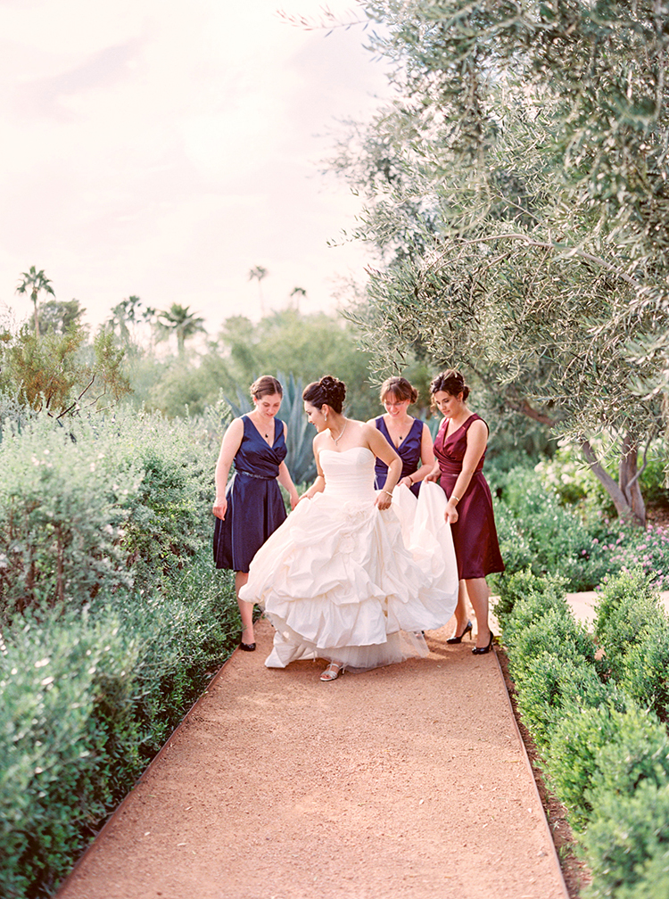 Jewel toned bridesmaids helping bride with dress before ceremony 