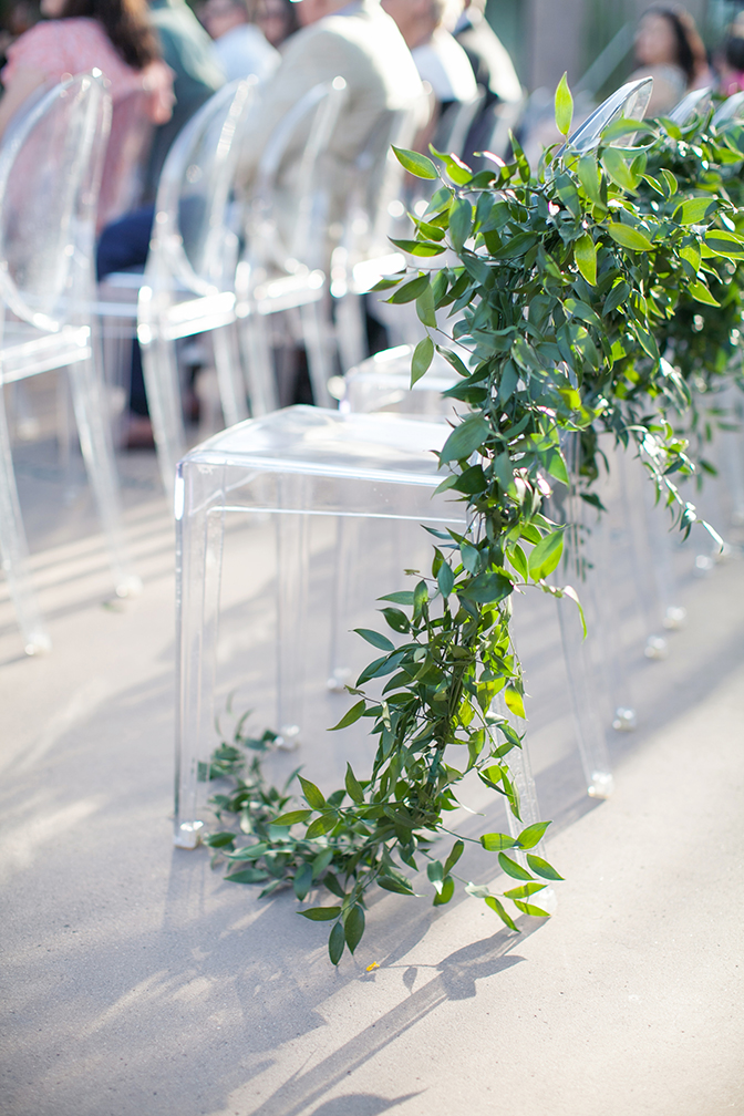 Clear acrylic chairs with garlands of greenery. Outdoor wedding ceremony decor.