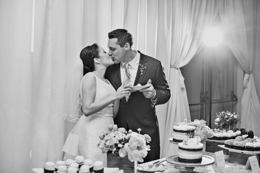 Bride & groom his after cutting the cake. Wedding reception desert table.