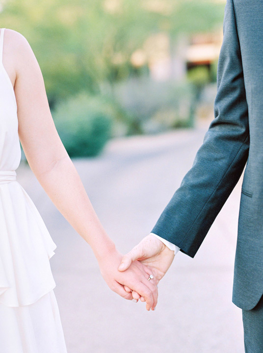 Bride and groom hold hands showing off the bride's diamond engagement ring.