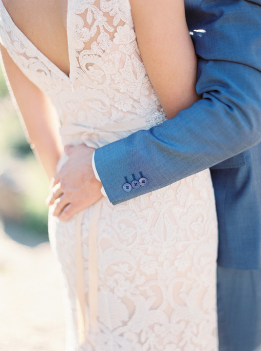 Groom embraces his bride in a beautiful lace detailed wedding dress.  