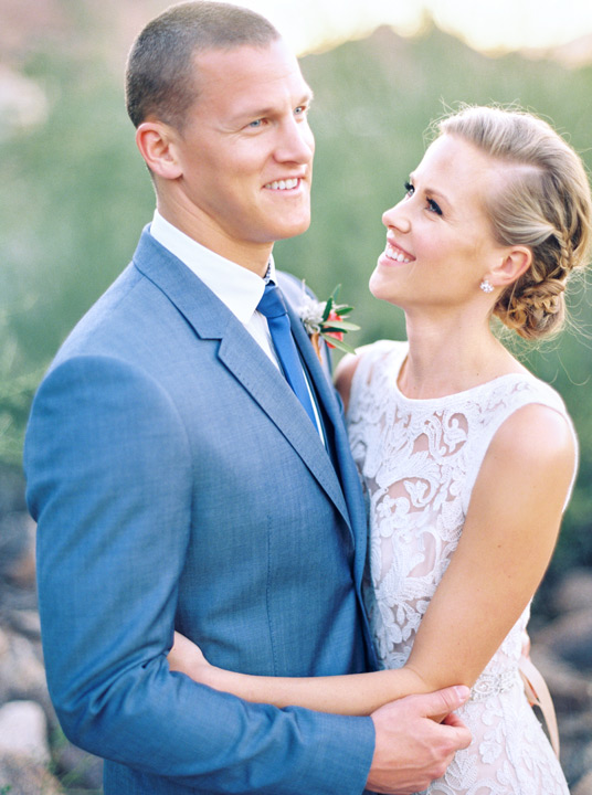 Bride and groom smile at each other on their wedding day. Blue suit and white lace wedding dress. 