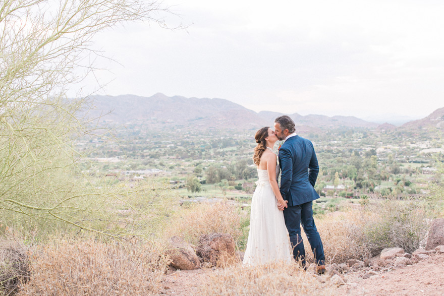 Bride and groom kiss with beautiful desert and mountain backdrop. Sanctuary on Camelback in Arizona.