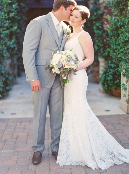 Bride in gorgeous lace wedding dress as her groom kisses her cheek sweetly. Wedding bouquet ideas. 