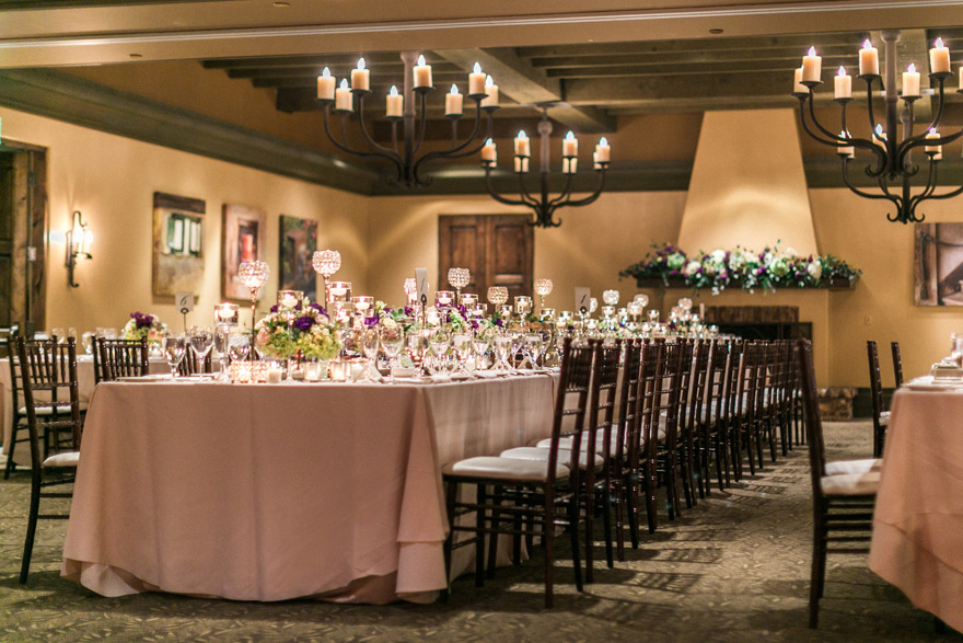 Indoor wedding reception table set up with blush table cloth and dark wood chairs. 