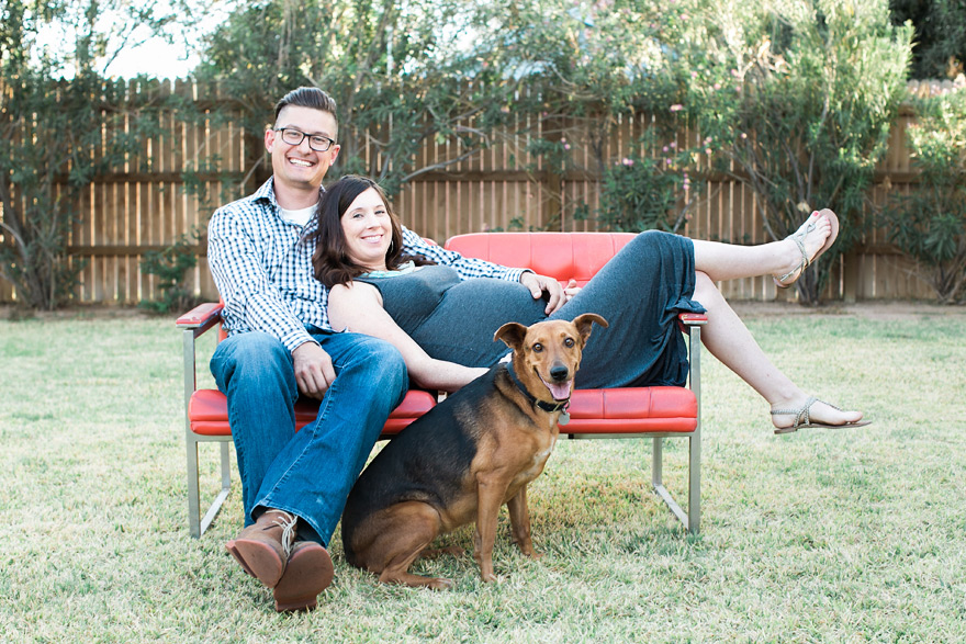 Couple lounging on red sofa with dog. Small family outdoors.