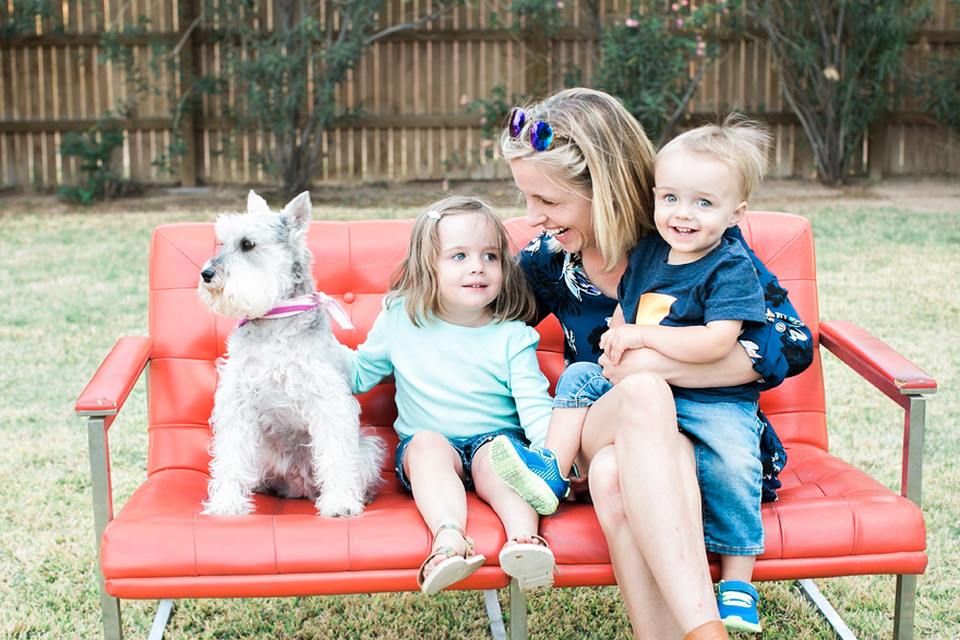 Mom laughing with sweet children and puppy on outdoor sofa.