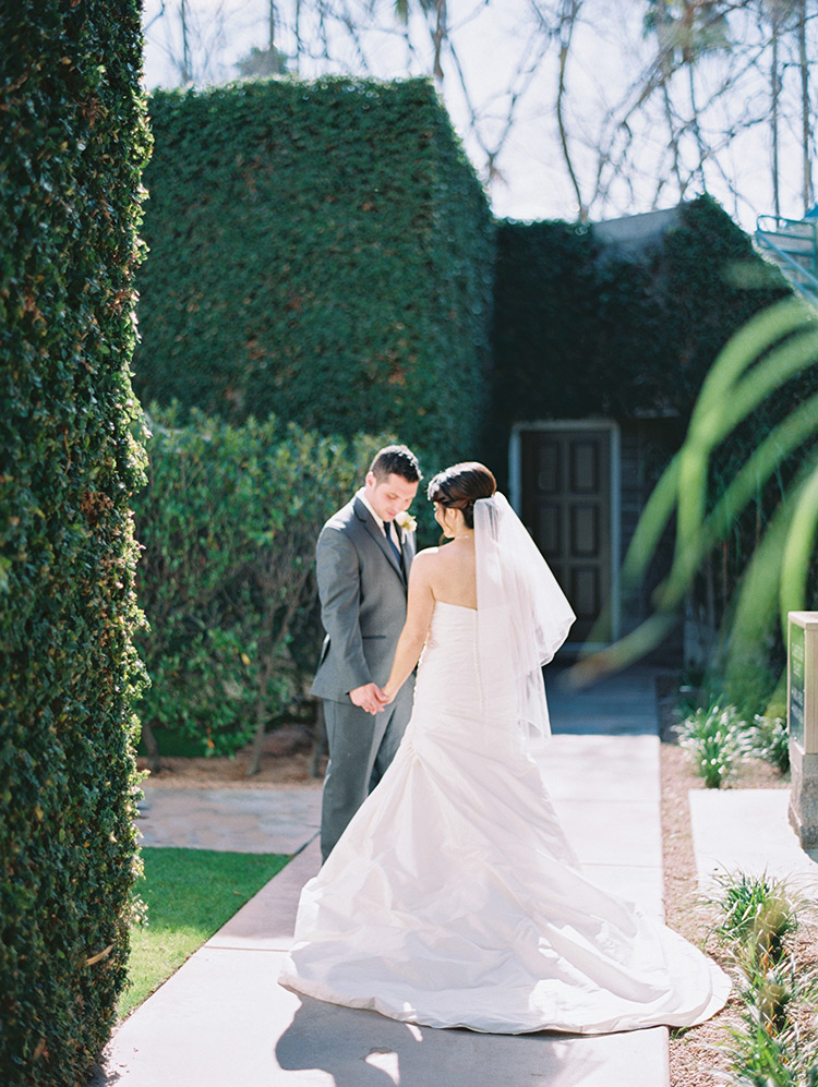 bride & groom hold hands in front of an ivy-covered wall 
