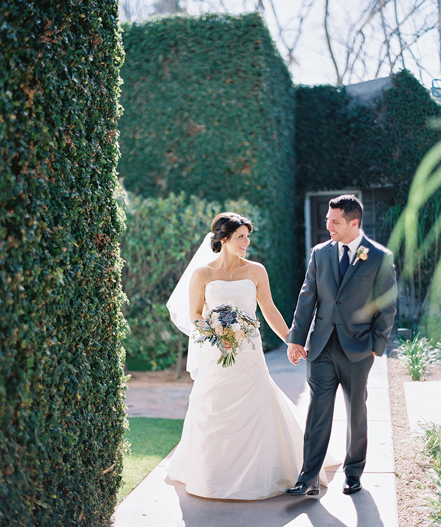 bride & groom hold hands in front of an ivy-covered wall 