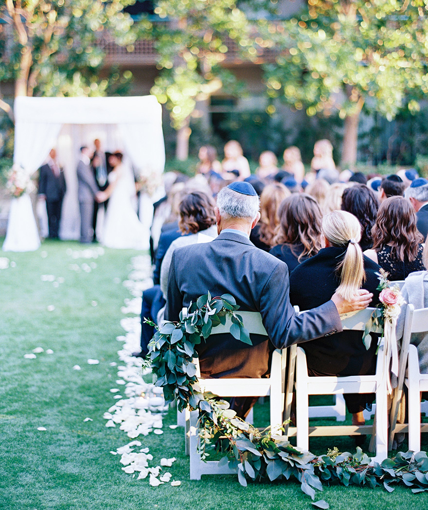 guests watch an outdoor wedding ceremony, chuppah