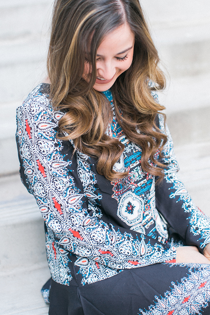 Patterned dress. Hair curled of girl sitting down taking a relaxed smiling picture. 
