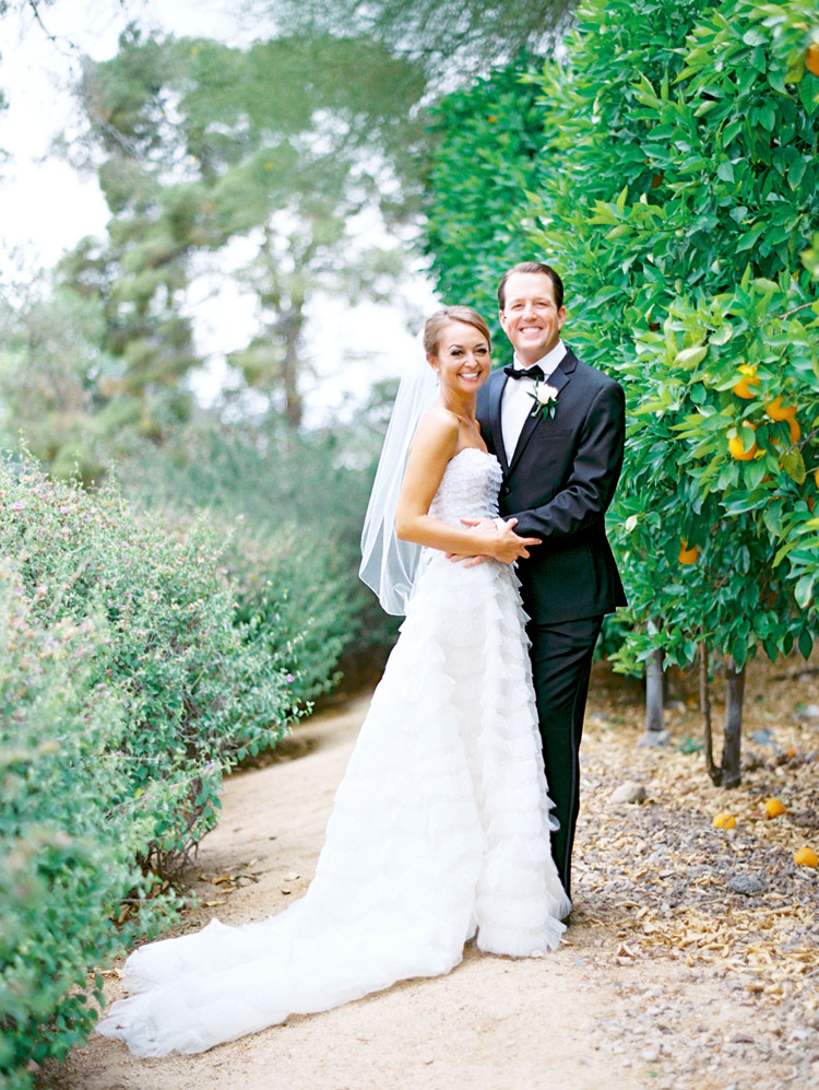 Bride & groom embrace beside an orange grove. Arizona wedding