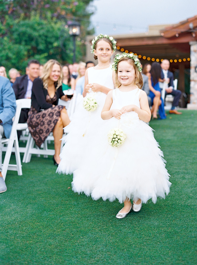 Flower girls in white ruffled dresses  carrying pomanders.
