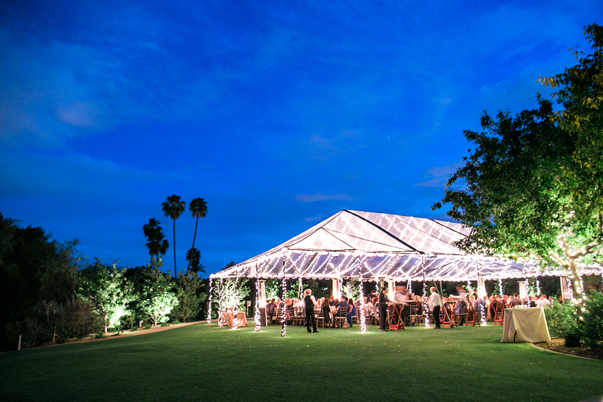 Clear tent glows with lights in the desert twilight. Outdoor wedding reception