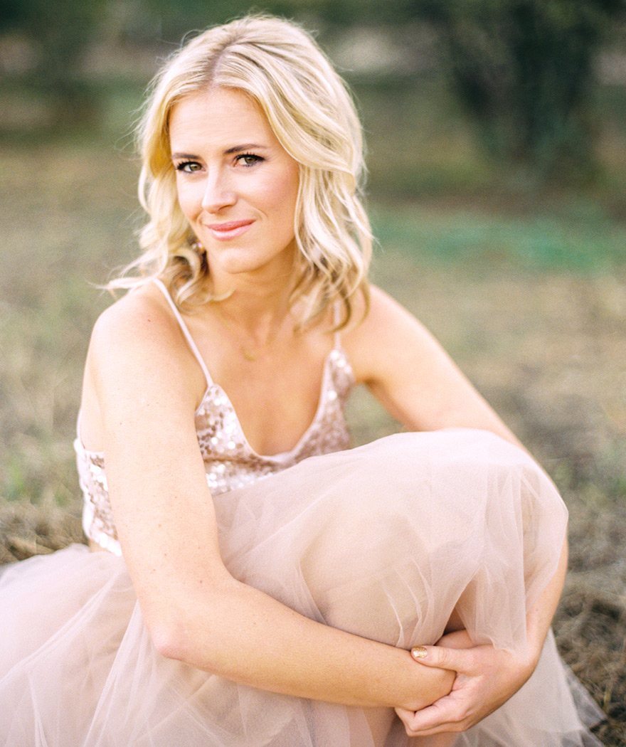 Soft smile of blonde cradling legs, outdoor blush session. 