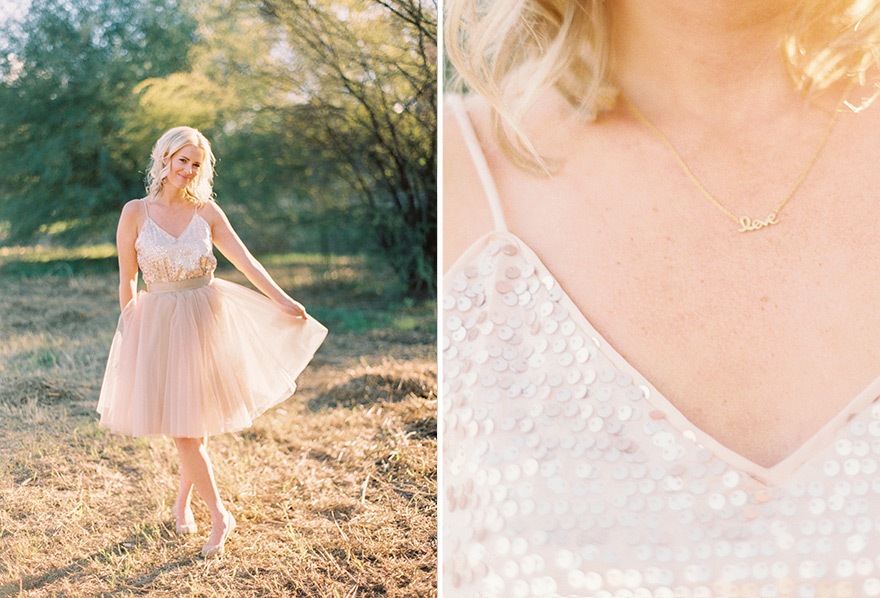 Graceful blonde holds blush tulle dress outdoors. Delicate, gold love bar necklace.  