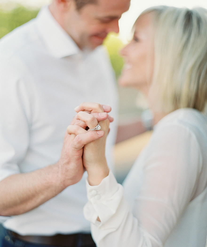 Couple share special moment holding hands portraying brides ring as they face one another 