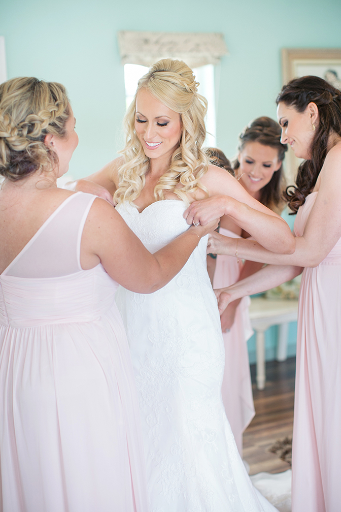 Bridesmaids helping beautiful blonde bride into her strapless wedding dress. Wedding inspiration.