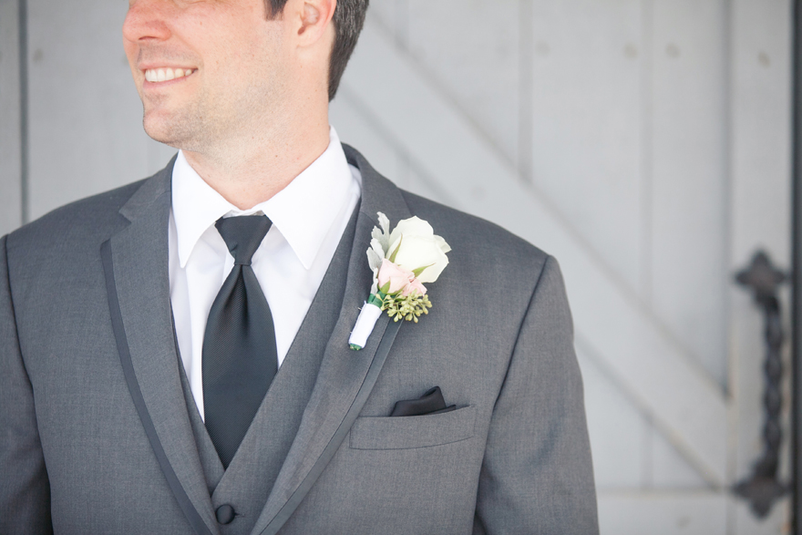 Groom portrait with white rose boutonniere and grey suit jacket. Wedding day photography.