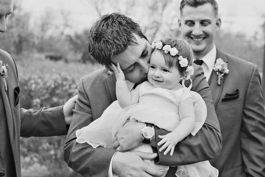 Groom kisses his baby daughter in adorable dress and floral crown. Wedding day photography ideas.